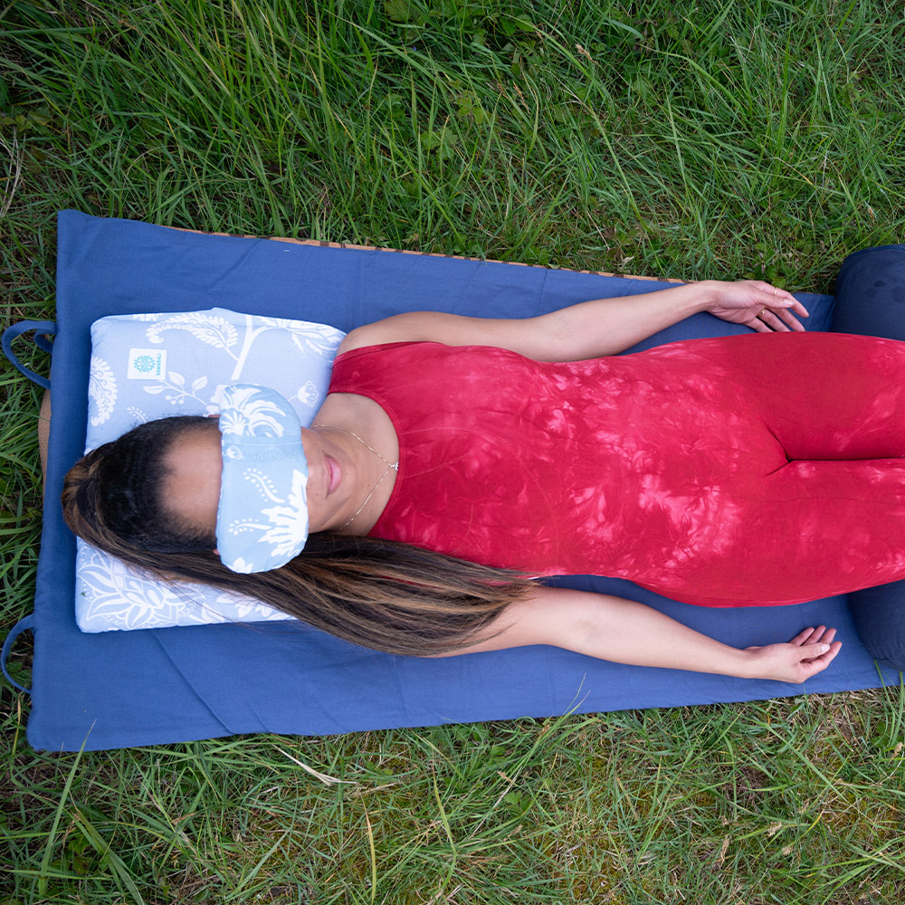 Ein Mädchen, das auf einer Yogamatte aus Baumwolle liegt und ein Augenkissen benutzt