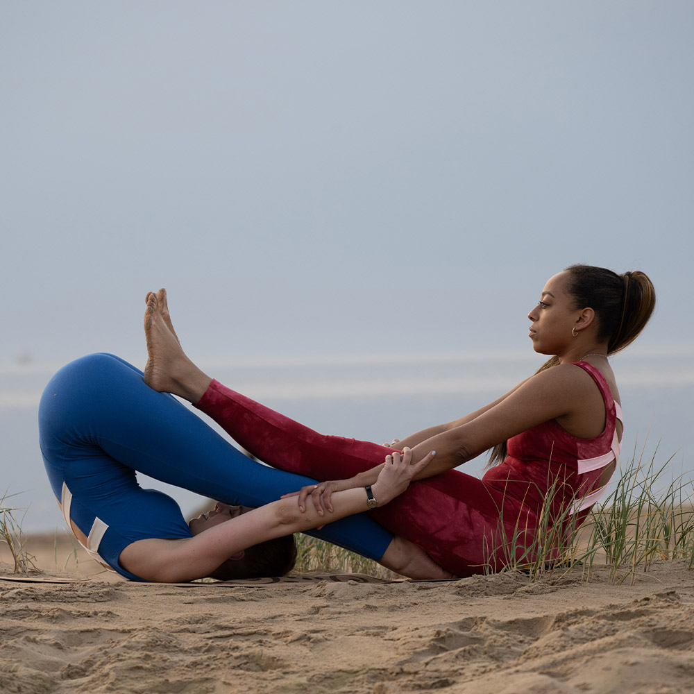 Two people yoga asana Two people exercising yoga on the beach. They are wearing jumpsuits of Samarali brand