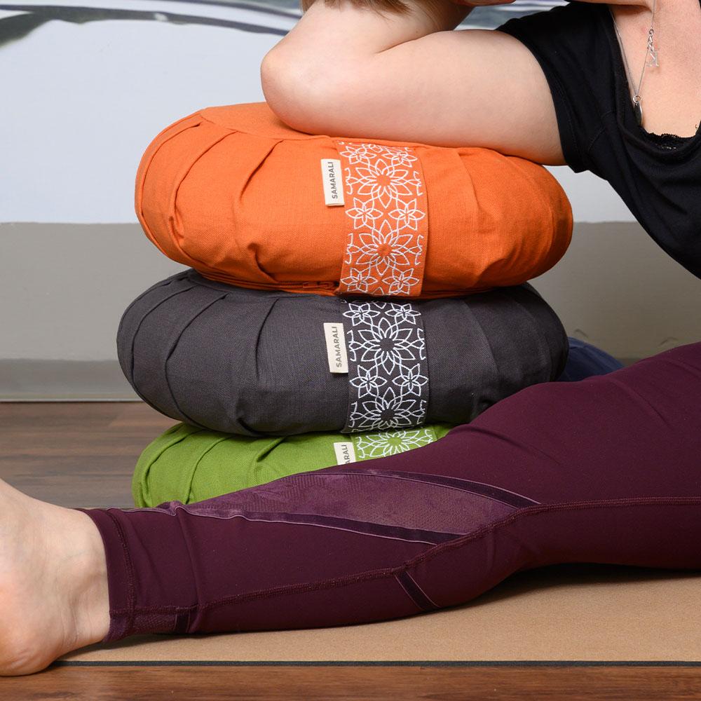 Zafu-kussen-sinaasappel Een zafu-meditatiekussen in oranje, grijs en groen, met daarop een vrouw die ertegenaan leunt