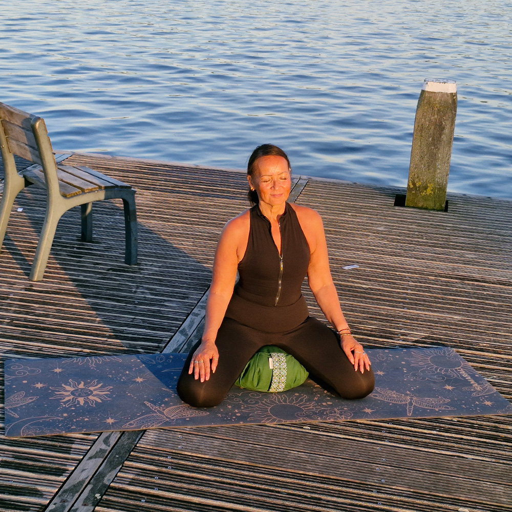 A female meditating sitting on meditation cushion zafu and a cork yoga mat Cosmic Harmony Cork Yoga Mat cork yoga mat